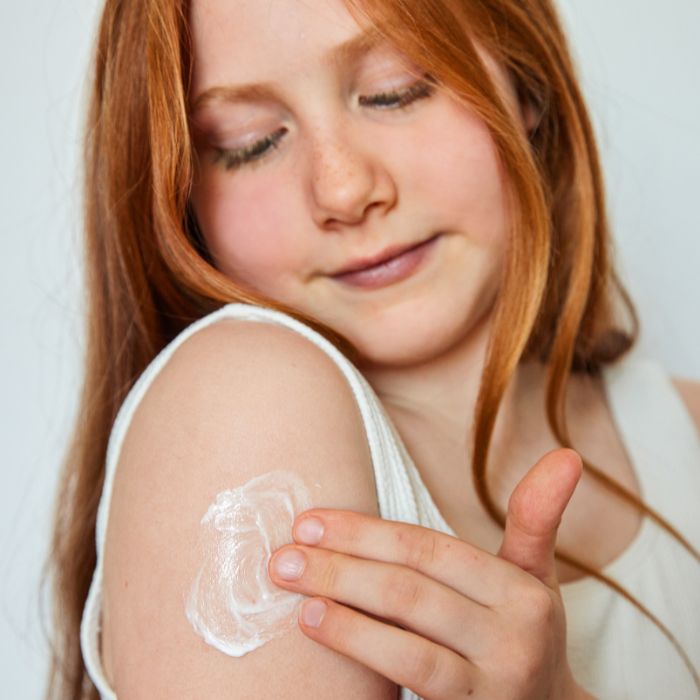 Jeune fille avec une peau atopique qui s'applique du baume émollient DA PROTECT sur la peau 